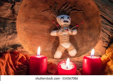 A voodoo doll with needles stands on an altar with candles
