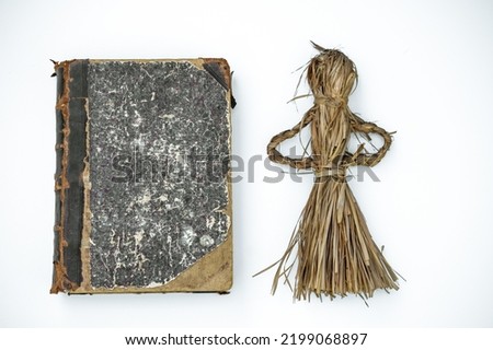 A voodoo doll and an old book on magic on white isolate. Tools for witchcraft. Witchcraft attributes. Straw doll on a white background.