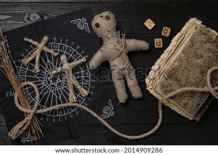 Voodoo doll with pins surrounded by ceremonial items on black wooden table, flat lay