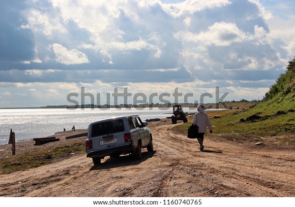 Vorogovo, Krasnoyarsk region/ Russia -\
08.13.2018: A woman walking and Lada car driving  by country road\
along the bank of the Yenisei River. in\
Siberia