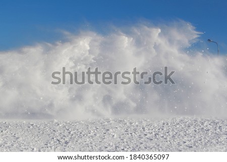 Vortexes of snow during the blizzard on blue sky background in the region of the far North. The theme of a natural disaster and the harsh polar climate. Typical picture of a northern winter. 

