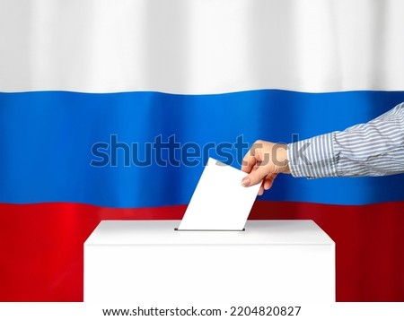 Voter's hand drops the ballot into the ballot box. Against the background of the Russian flag. Filling out ballots and a referendum in Ukraine. The concept of elections
