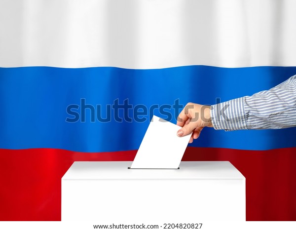 Voter\'s hand drops the\
ballot into the ballot box. Against the background of the Russian\
flag. Filling out ballots and a referendum in Ukraine. The concept\
of elections