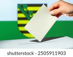 Voting envelope is put into ballot box for state elections in Saxony. grey envelope in hand. Flag of Saxony in the background. Election year 2024 in Germany.