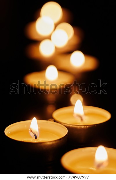 Votive candles burning in the darkness in a church
or during a remembrance vigil at night with shallow dof and
background bokeh