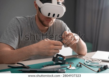 A vr engineer is focused on assembling a device using various tools and electronic parts on a work table at home.