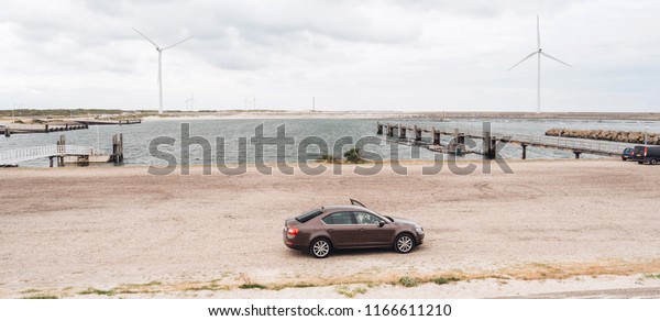 Vrouwenpolder,\
Netherlands - Aug 25, 2018: Luxury Skoda car parked in the bay -\
elevated view - rainy cloudy netherlands weather and big wind\
turbines for the elctric hybrid\
car