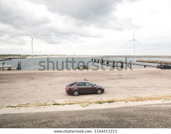 Vrouwenpolder,\
Netherlands - Aug 25, 2018: Luxury Skoda car parked in the bay -\
elevated view - rainy cloudy netherlands weather and big wind\
turbines for the elctric hybrid\
car