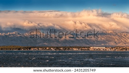 Vrsi, Croatia - Panoramic view of Vrsi municipality in Zadar county with Velebit mountains and Paklenica national park covered with warm golden colored clouds and rainbow in background at sunset Stock photo © 