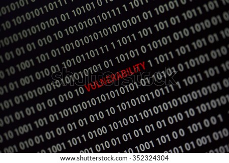 'Vulnerability' word in the middle of the computer screen surrounded by numbers zero and one. Image is taken in a small angle.
