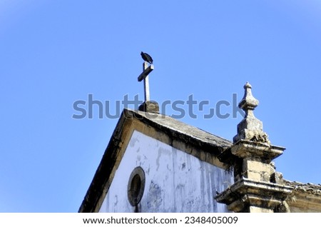A vulture resting peacefully on the tip of the cross in the church in Paraty