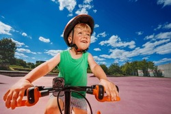 W Low Angle Portrait Of A Little Blond Smiling Boy Ride Small Bicycle On Color Surface Of The Park