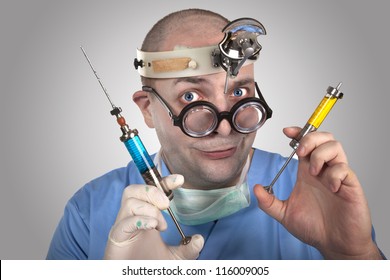 Wacky doctor with two syringes ready to give an injection. Funny young man in surgeon outfit with  crazy glasses and head mirror