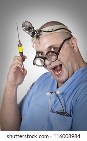 Wacky Smiling Doctor With A Syringe And Crazy Glasses. Young Man In Doctor Outfit Holding Syringe With Yellow Medicine