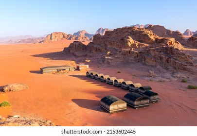 Wadi Rum desert, Jordan. Beautiful aerial view of bedouin camp at sunset from above with tents lined up and red rock formations landscape.