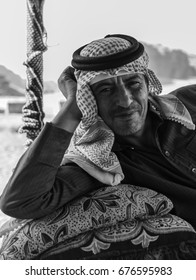 Wadi Rum, Jordan - June 20, 2017: Bedouin Man Or Arab Man In Traditional Outfit, Lying Down On The Couch, Desert Background.