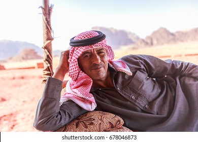 Wadi Rum, Jordan - June 20, 2017: Bedouin Man Or Arab Man In Traditional Outfit, Lying Down On The Couch, Desert Background.