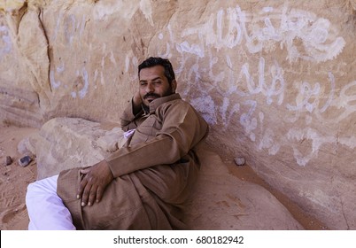 Wadi Rum, Jordan - June 20, 2017: Bedouin Man Or Arab Man In Traditional Outfit, Lying Down On The Rock.