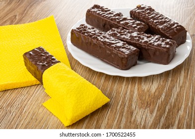 Wafer Wrapped In Napkin On Yellow Paper Napkins, Wafers In Chocolate Glaze In White Glass Plate On Wooden Table