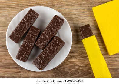 Wafers In Chocolate Glaze In White Glass Plate, Wafer Wrapped In Napkin, Yellow Paper Napkins On Wooden Table. Top View