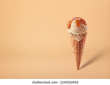 Waffle cone of caramel ice cream scoop with sauce on brown background. Space for text. Foto Stok