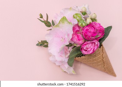Waffle cone with composition of beautiful blooming hydrangea and roses flowers and branches on pink background.  Flat lay 