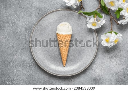 Waffle cone with ice cream on the plate and decorative blossoming cherry branch, gray concrete background. Top view, flat lay.