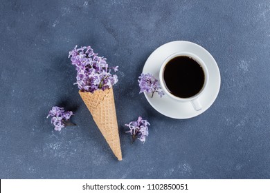 Waffle cone with purple lilac and cup of black coffee on dark blue stone concrete table background. Flat-lay, top view, copy space. Morher Day Holiday Concept - Powered by Shutterstock