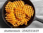 Waffle criss cross fries in a cast iron frying pan on a wooden cutting coard. Unhealthy fast food concept