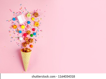 Waffle horn with colored candy, sweets, marshmallow, caramel popcorn, sweet powder on a pink background. Top view, sweets and candy concept. Copy space