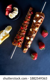 waffle sticks, 2 sticks glazed with chocolate and fruits, strawberries and bananas, black background 