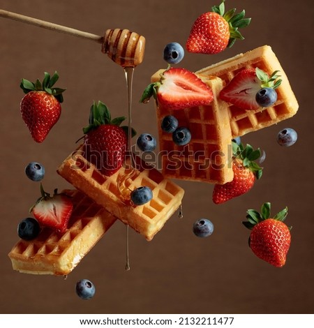 Waffles with blueberries and strawberries are watered with honey. Food levitation.