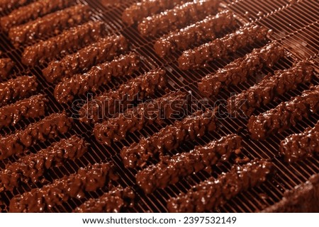 Waffles with nuts are coated with chocolate on conveyor. Production line of food factory, concept modern bakery plant.