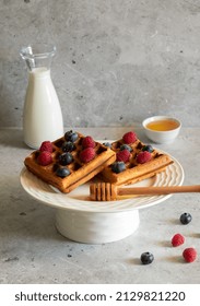 Waffles with raspberries, blueberries and honey on a light concrete background