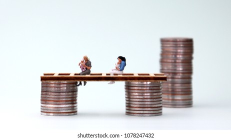 A miniature woman holding a baby and a pile of coins. Wage Freeze Concept For Women.