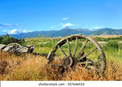 Wagon and wheels lay abandoned in deep grass along the highway in Paradise Valley, Montana.  The Absaroka Mountains loom in the distance.