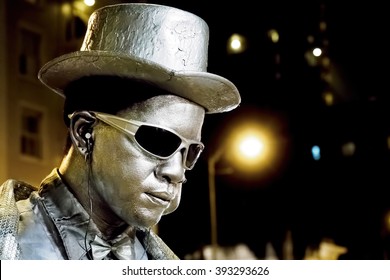 Waikiki, Honolulu, Hawaii, USA - Dec 12, 2015: Closeup Of A Night Street Performer Keeping Still. His Face Is Painted Silver To Match His Clothing Color. People Watch In Awe And Often Donate Money.