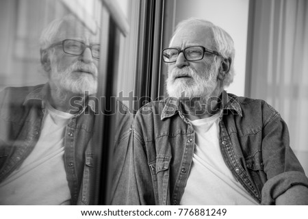 Waist up black-and-white portrait of thoughtful bearded man expressing nostalgia while resting. He is squinting eyes