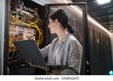 Waist up of female network engineer connecting cables in server cabinet while working with supercomputer in data center, copy space - Powered by Shutterstock