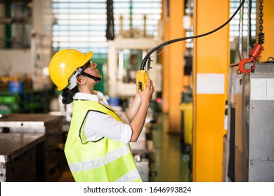 Waist up female worker uses remote control panel for lifting down power trolley crane in factory warehouse. Asian woman controls crane beam in manufacturing facility. - Powered by Shutterstock