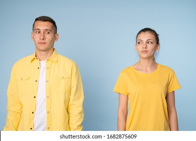 Waist Up Photo Of A Confused Couple In Yellow Shirts Looking At Each Other, Isolated Over Blue Background