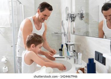 Waist up photo of smiling father and happy little son washing their hands together near the sink at home
