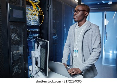 Waist up portrait of adult black man working as IT engineer using laptop while setting up internet network in server room