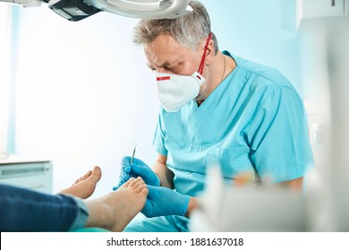 Waist Up Portrait Of Adult Man In Uniform And Gloves Is Doing Pedicure Procedure While Patient Sitting On The Medical Chair In Beauty Clinic