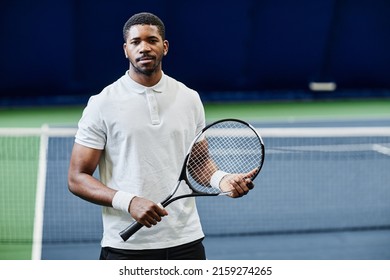 Waist up portrait of African American tennis player looking at camera while posing confidently with racket at indoor court, copy space - Powered by Shutterstock