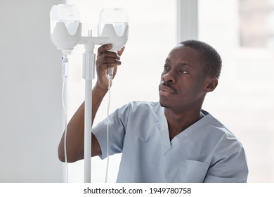 Waist up portrait of African-American male nurse setting up IV drip while treating patients in hospital, copy space - Powered by Shutterstock