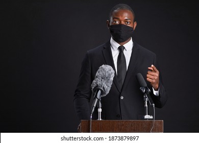 Waist Up Portrait Of African-American Man Wearing Mask While Giving Speech Standing At Podium Against Black Background, Copy Space