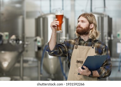 Waist up portrait of bearded brewmaster holding beer glass while inspecting quality of production at brewing factory, copy space - Powered by Shutterstock