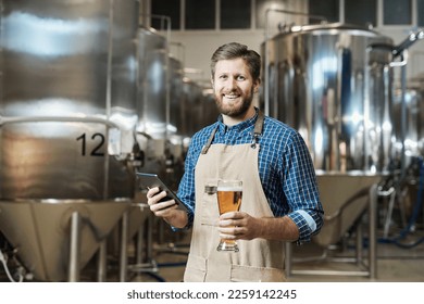 Waist up portrait of bearded brewmaster holding beer glass and looking at camera while standing at brewing factory - Powered by Shutterstock