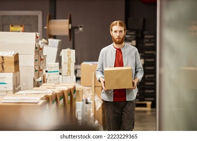 Waist Up Portrait Of Bearded Young Man Carrying Box And Walking Towards Camera In Workshop Or Supply Room, Copy Space